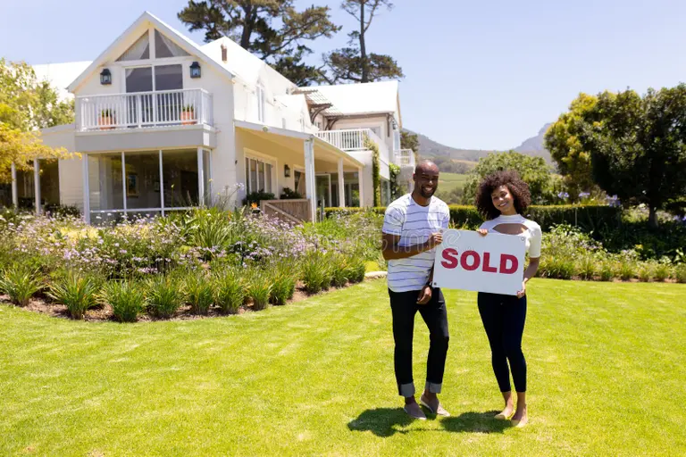 Happy first-time home buyers holding a SOLD sign in front of their new Gwinnett County home